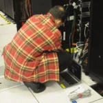 Techniker mit Laptop arbeitet an der Verkabelung eines offenen 19-Zoll-Racks