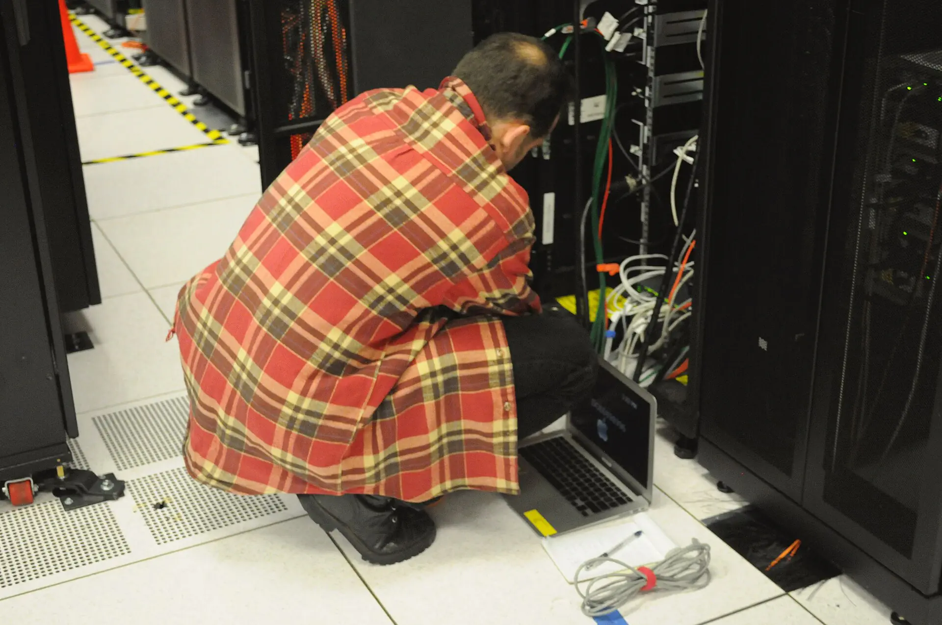 Techniker mit Laptop arbeitet an der Verkabelung eines offenen 19-Zoll-Racks
