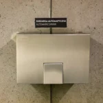 Händetrockner aus gebürstetem Edelstahl an einer Betonwand in einem öffentlichen Waschraum